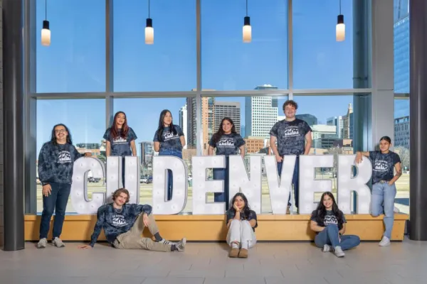 Students in blue shirts and blue jeans stand around a CU Denver sign