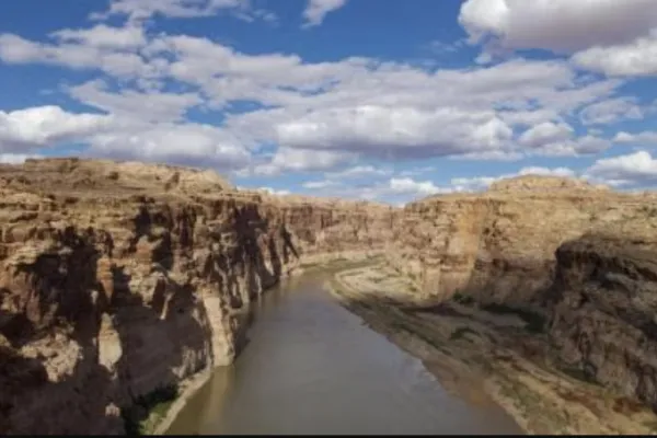 A river flows through a canyon, blue skies and clouds above