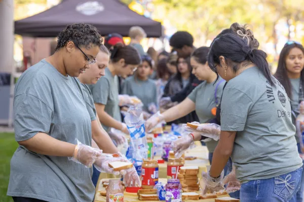 Student volunteers in blueish gray tshirts mill around a table preparing meals