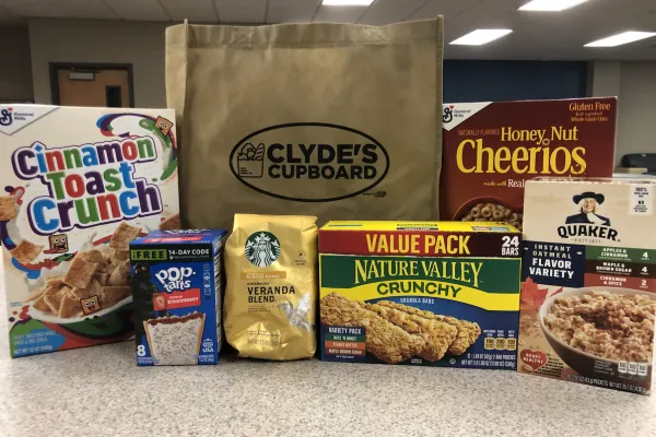 Boxed cereal and dried goods on a kitchen counter top, a paper bag with the Clyde's Cupboard logo in the center