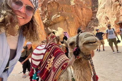 A photo of Sara Khammash wearing sunglasses and posing with a camel in a desert setting