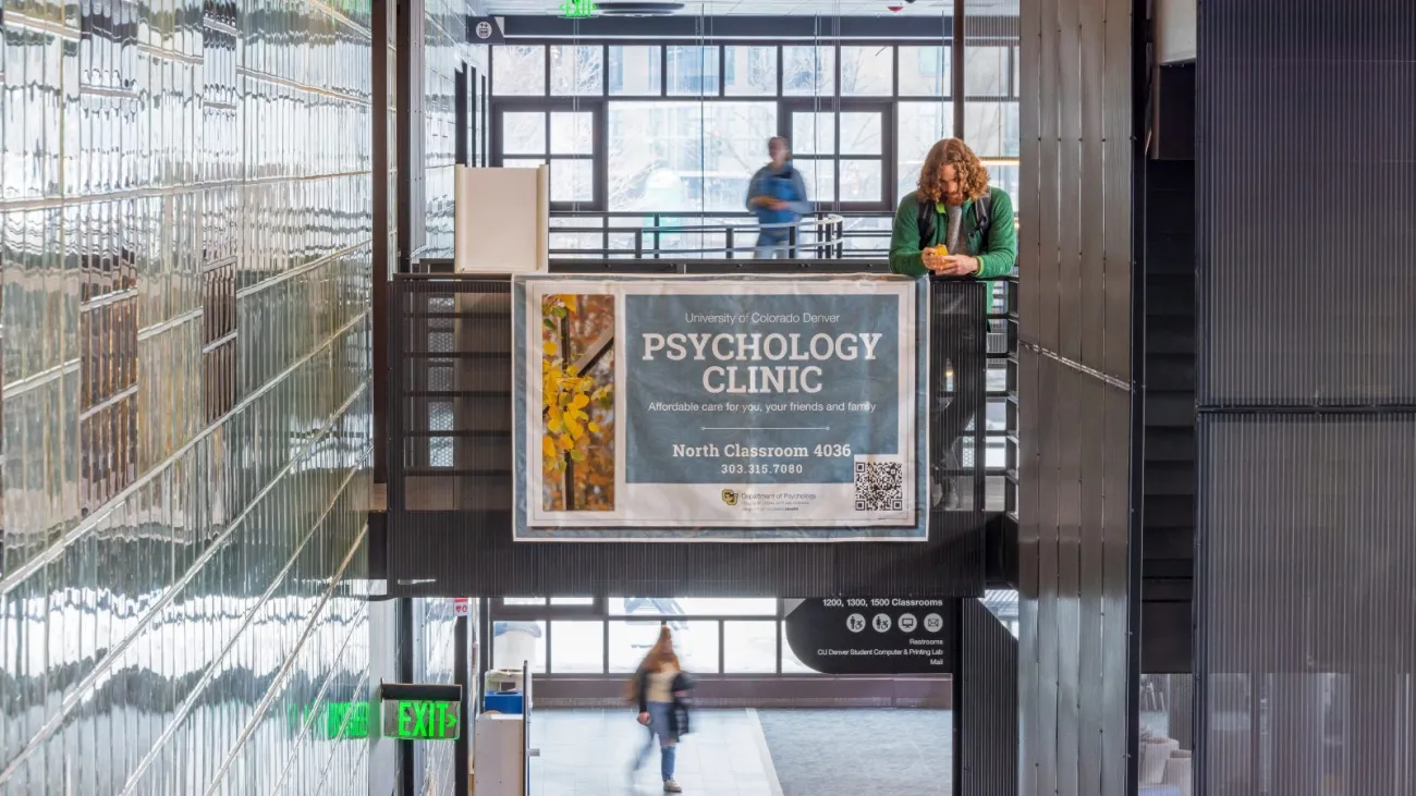 A light-filled interior of a CU Denver building with a banner advertising the CU Denver Psychology Clinic